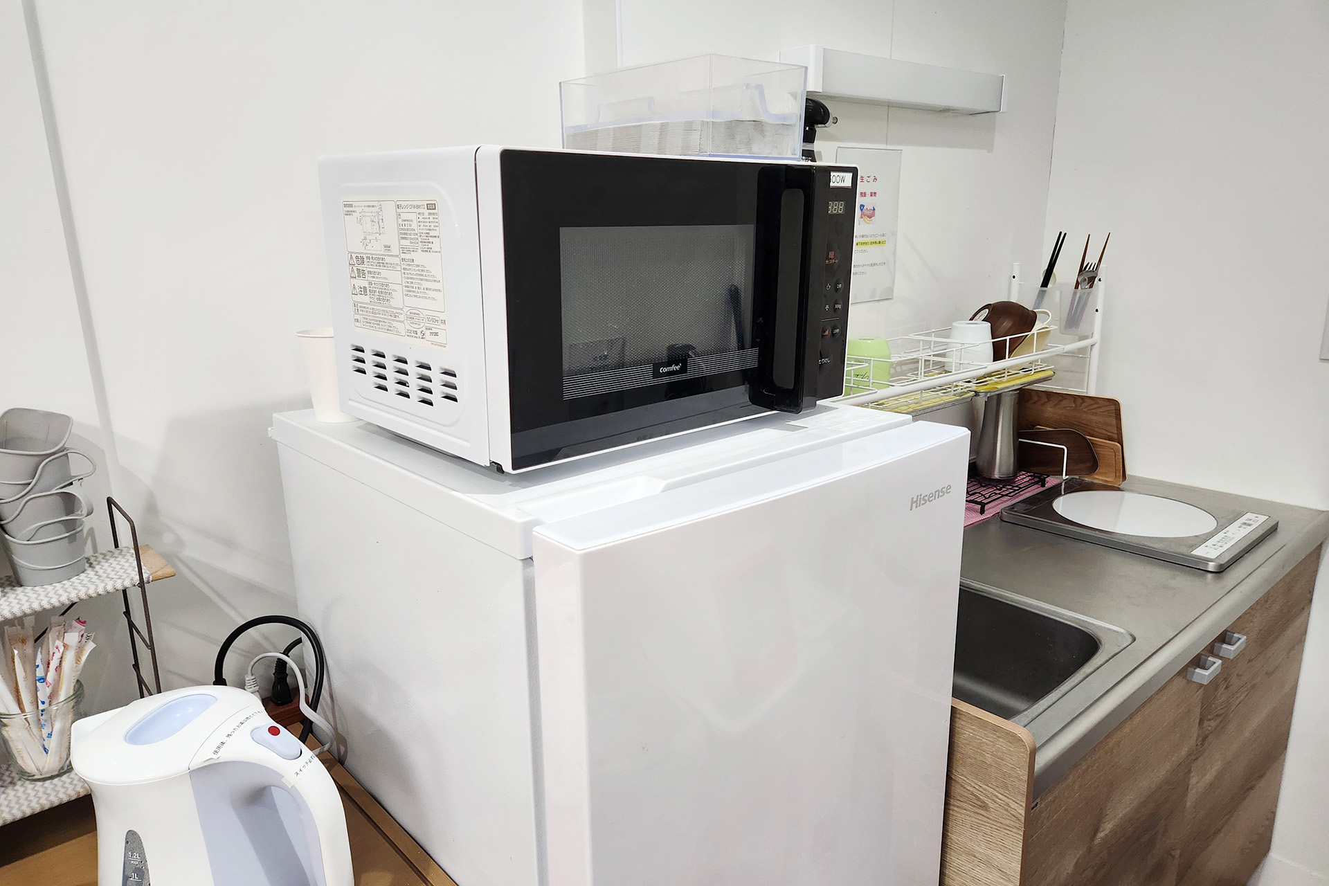 出入口付近にある棚の奥に簡易的なキッチンがあり、冷蔵庫の上には電子レンジがあります