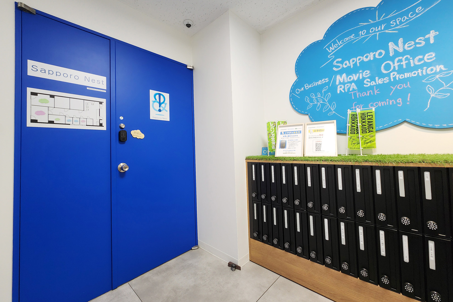 エレベーターを降りて左手に青い扉、右手に水色の看板がある。水色の看板には「SapporoNest」と書かれています