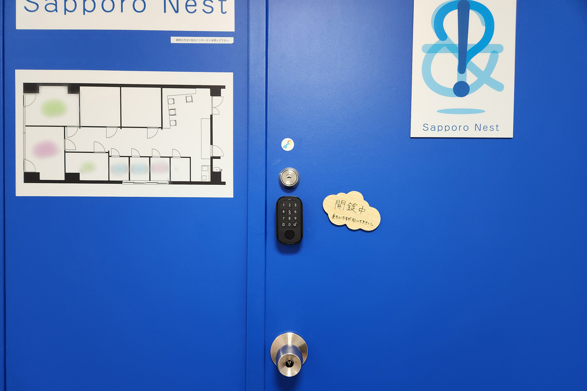 青い扉のドアノブ付近に黒くて小さい端末がある。この端末がスマートロックにあたります